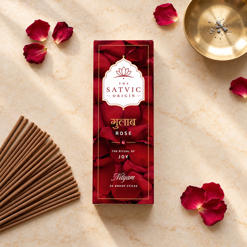 A box of Satvic Origin Niyam Rose shisha sticks is displayed in a styled flat-lay on a beige marble surface, surrounded by red rose petals, wooden sticks, and a brass incense burner.