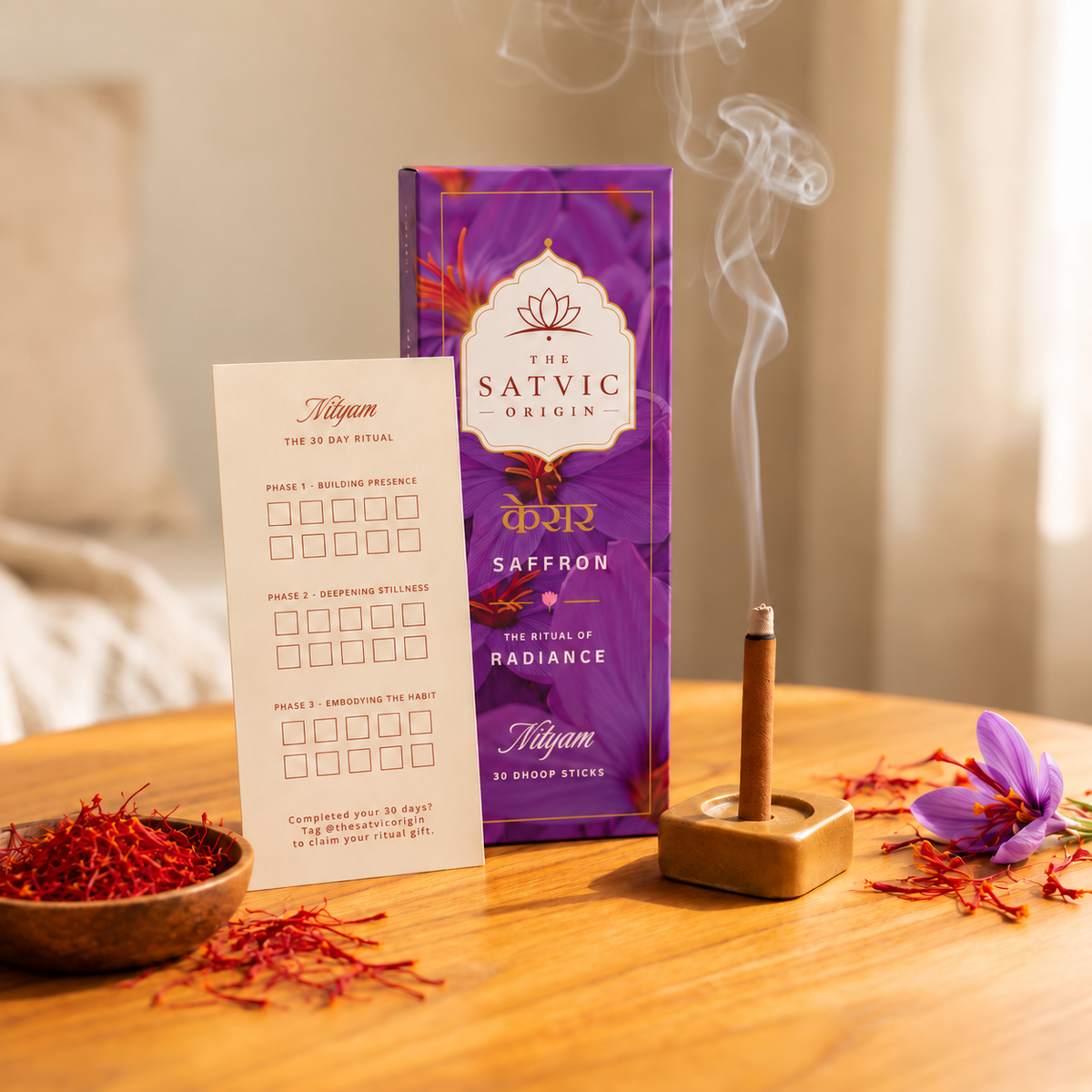 The Satvic Origin Saffron Pranayama set on a wooden table, featuring a purple box, a white practice card, a burning incense stick in a wooden holder with smoke rising, and a small bowl of red saffron threads with loose saffron petals scattered around.