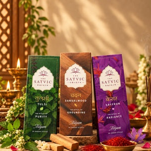 Three Satvic Organics incense sticks packages (Tulsi, Sandalwood, and Saffron) displayed in a warm, decorative setting with lit candles, incense sticks, and herbs.
